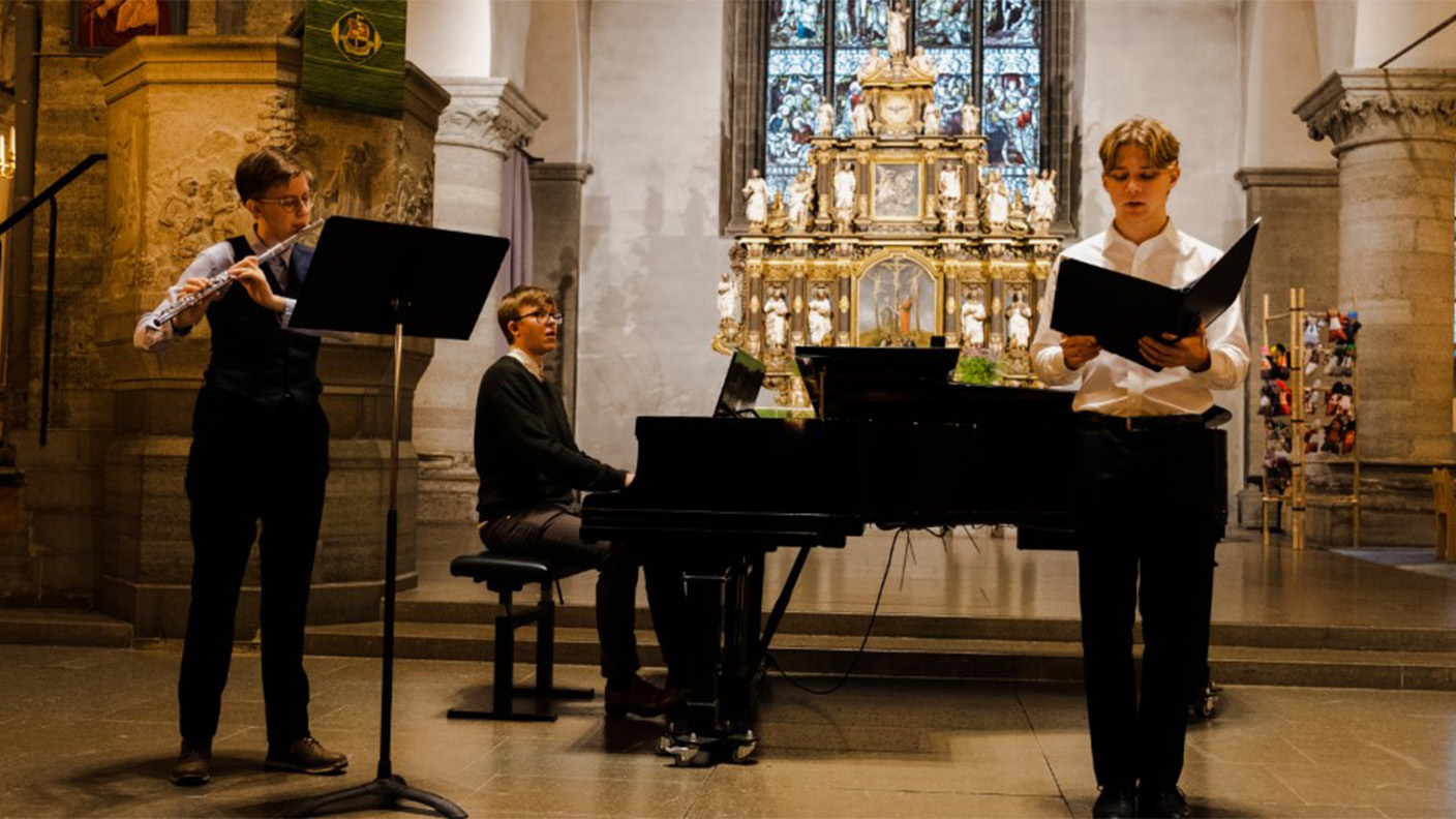 Tre unga män framför musik med piano, klarinett och sång i kyrka.