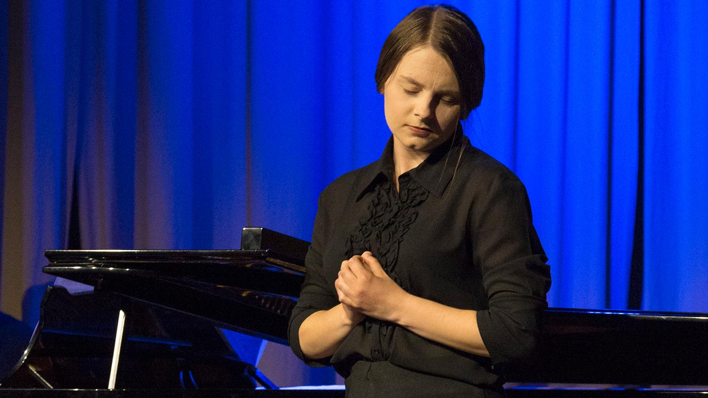 Linnea framträder på en scen som badar i blått och gult ljus. Hon vilar mitt i sången, huvudet på sned och med händerna knäppta framför bröstet. Hon är klädd i en lång svart klänning.