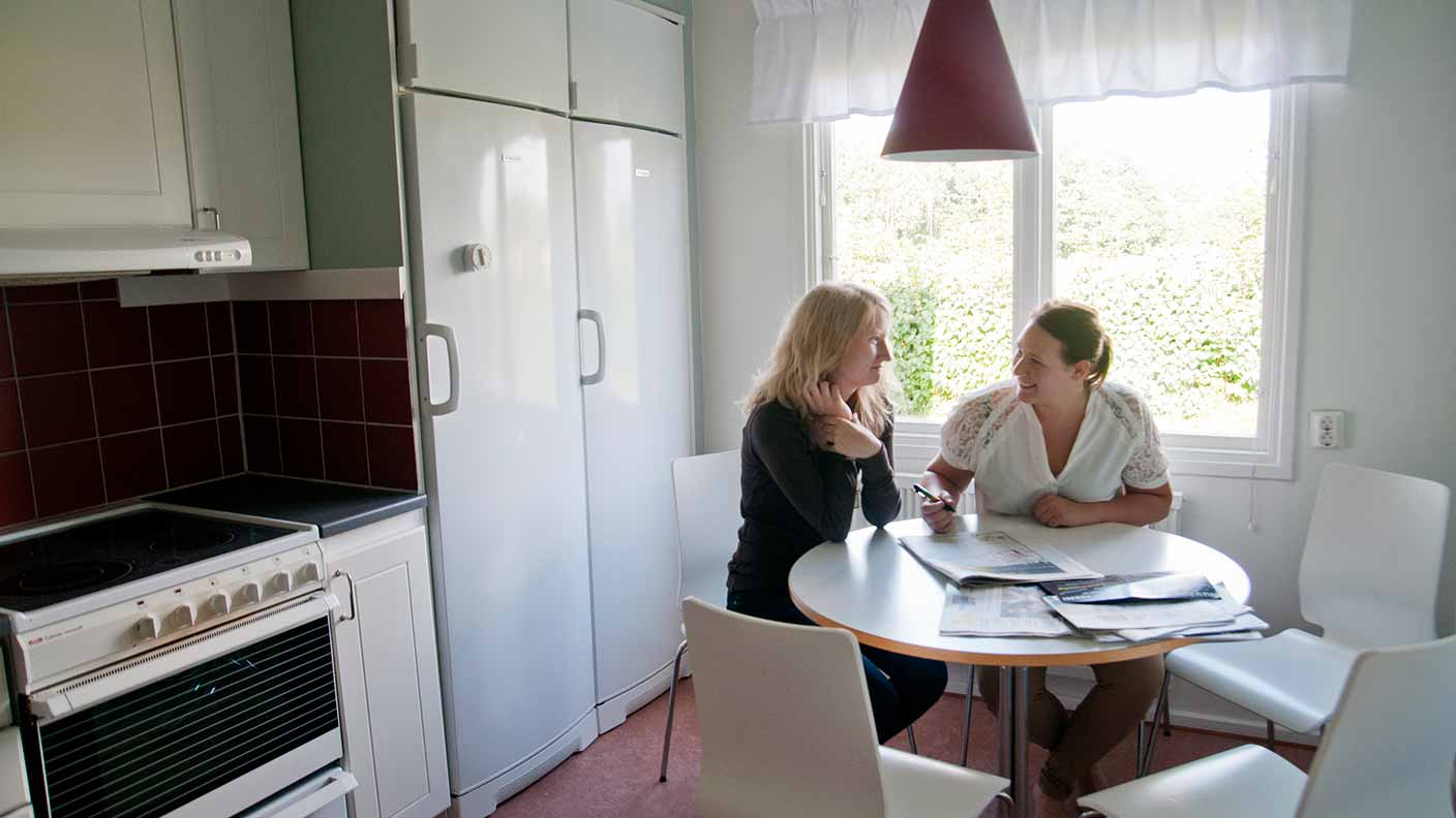 Två personer sitter vid ett runt vitt bord i ett litet gemensamt kök.