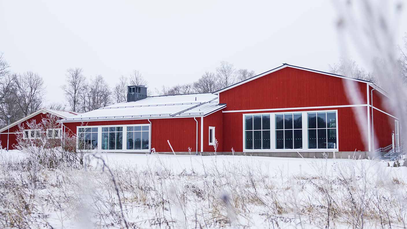 Danshuset syns i ett vitt och snöigt vinterlandskap. I förgrunden syns några kala buskar. Danshuset består av tre byggnader som är sammankopplade; alla med röd fasad och vita knutar. Huset har stora breda fönster som upptar större delen av de gavlar som syns på bilden.