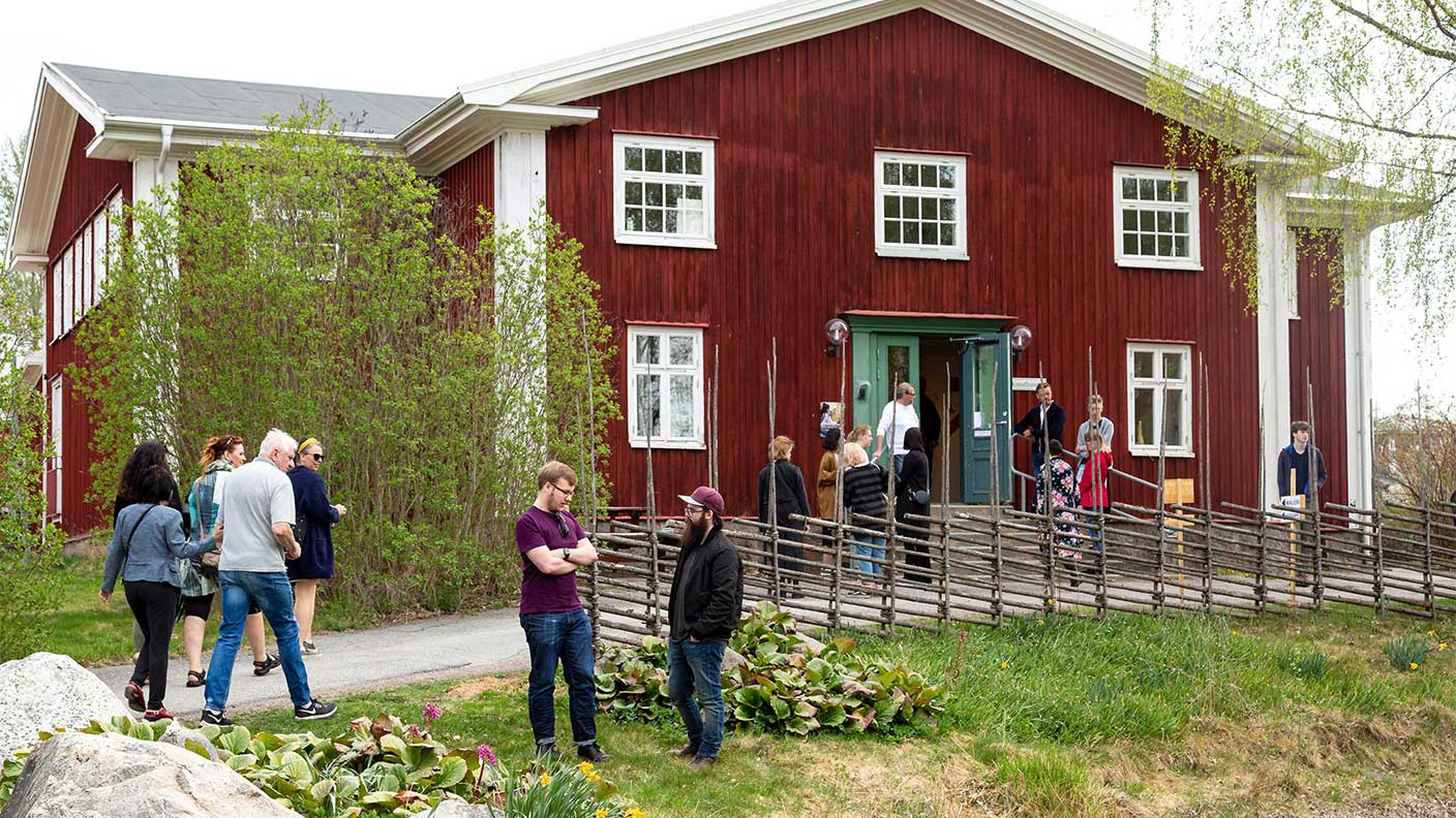 Konsthuset är ett rött tvåvåningshus med vita knutar. På bilden går flera grupper av människor förbi huset, eller står utanför och pratar.