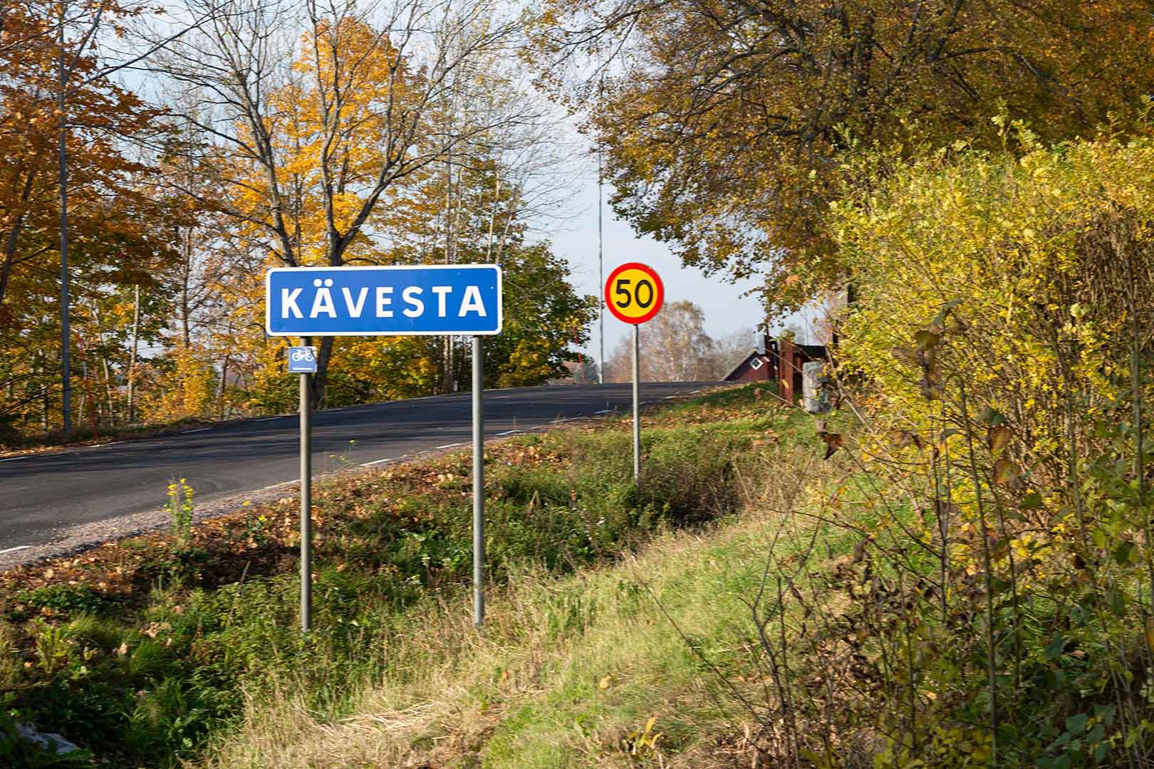 I förgrunden en blå vägskylt med texten Kävesta. Bakom den en röd och gul hastighetsskylt med texten 50.