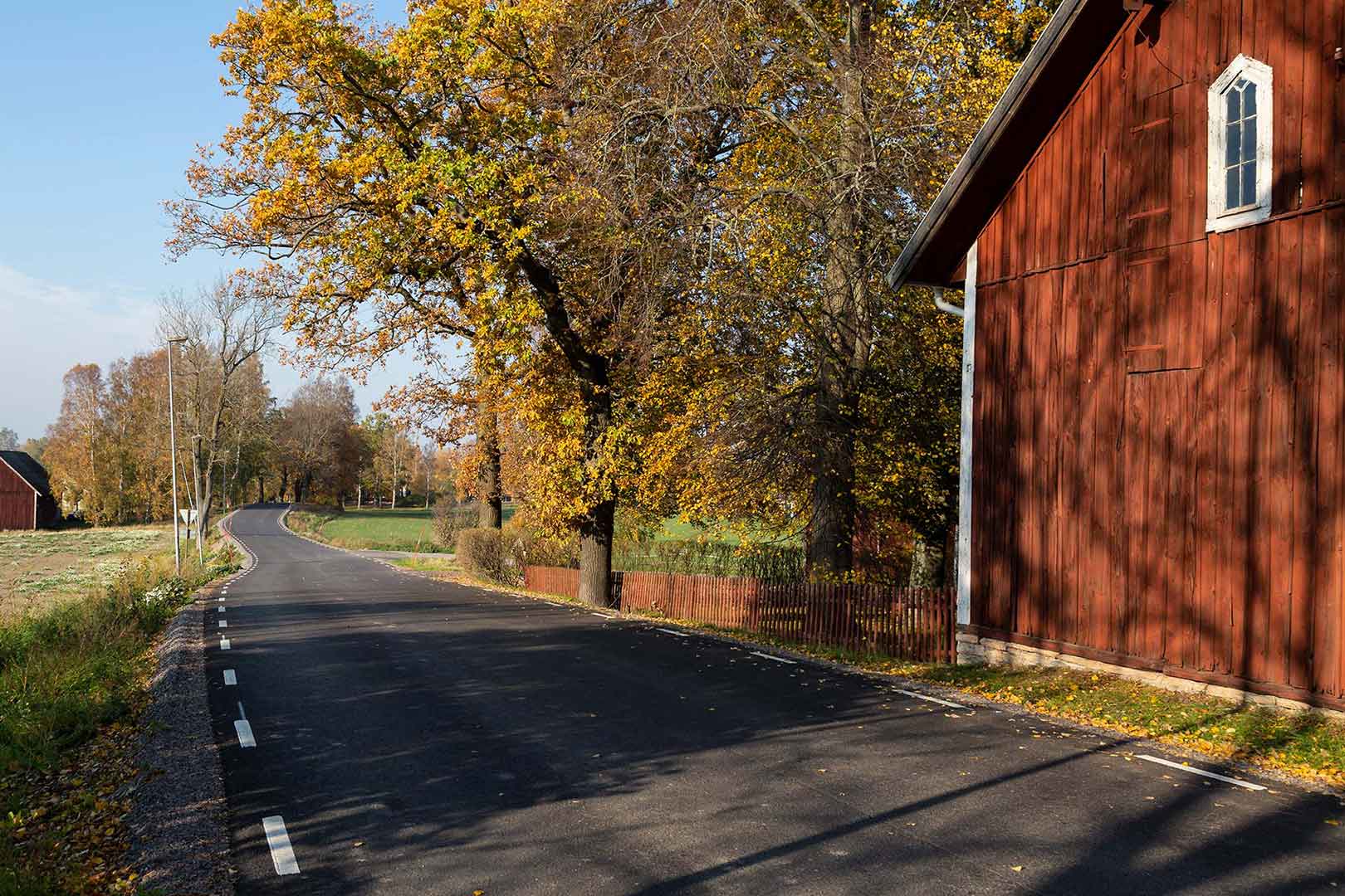 En bilväg leder rakt framåt. Till höger står en stor röd lada.