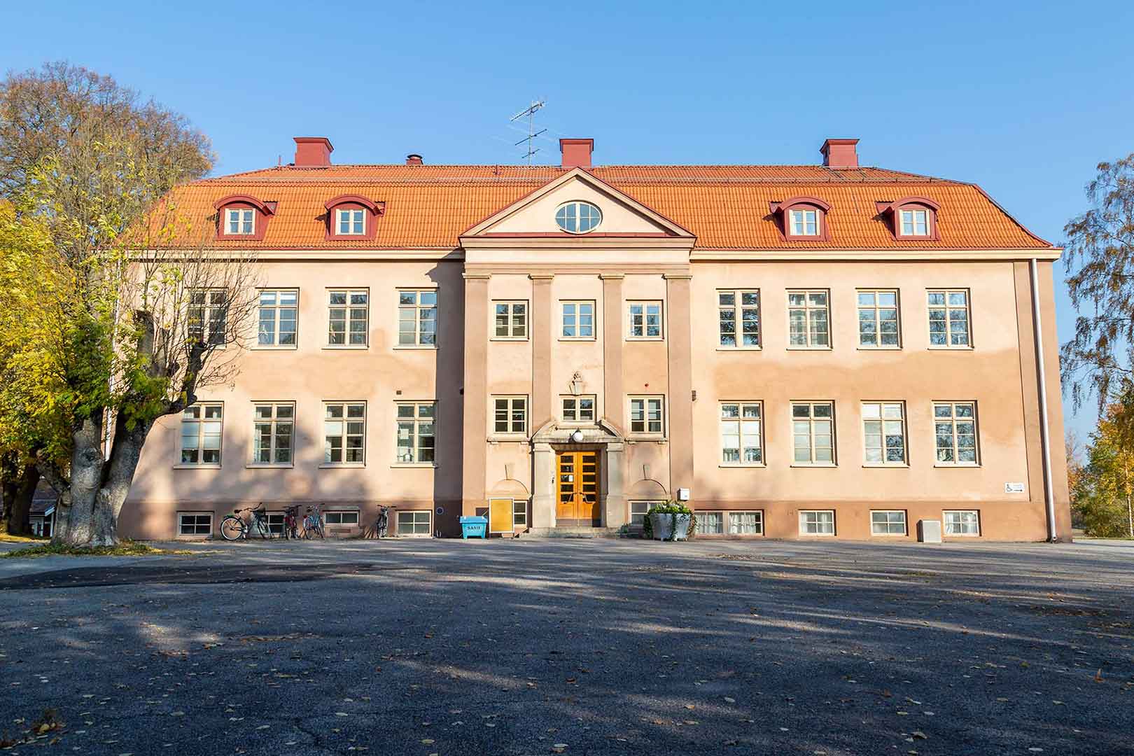 Stora skolhuset på håll - en tre våningar hög orange byggnad.